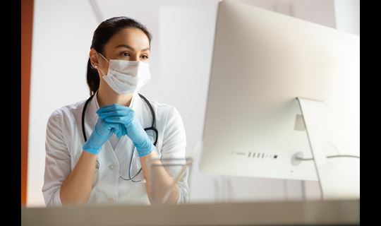 Masked healthcare professional watching computer